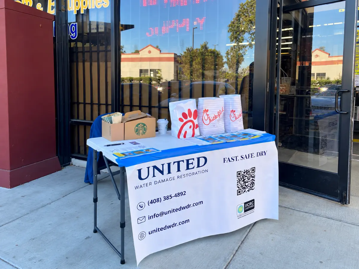 United Water Damage Restoration promotional table with brochures, refreshments, and company banner outside a storefront.