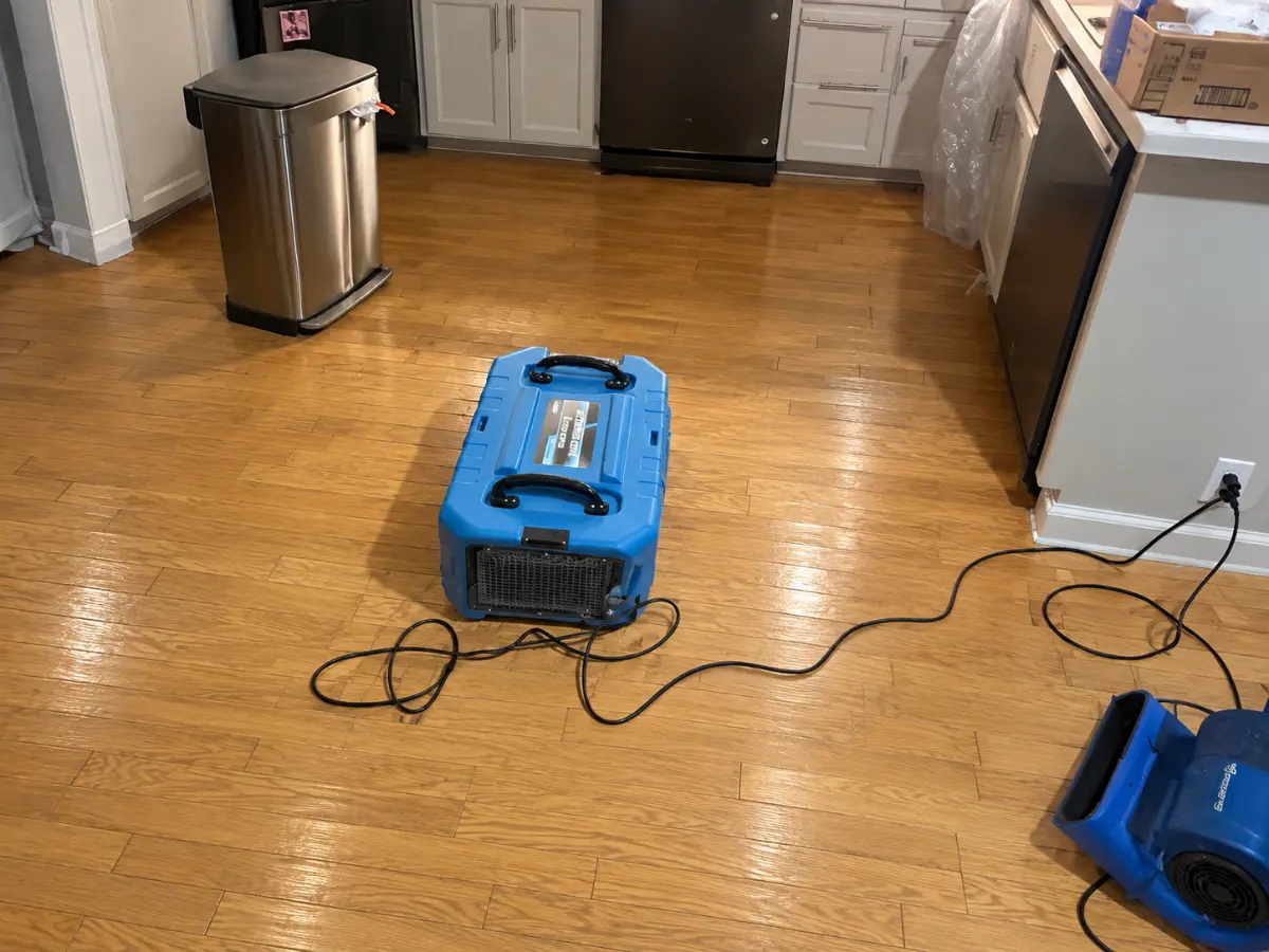 Dehumidifier and air mover drying hardwood flooring in a residential kitchen after water damage.